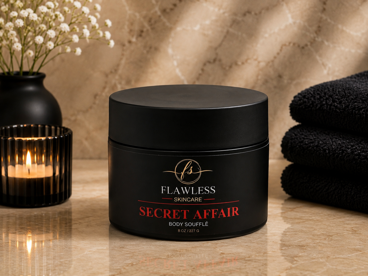This is a man’s scented body lotion with musk, amber, citrus, and woody notes. A black cosmetic jar labeled 'Flawless Skincare Secret Affair Body Souffle' sits on a polished stone surface, styled with a lit candle, flowers, and folded black towels in a warm bathroom-like setting.
